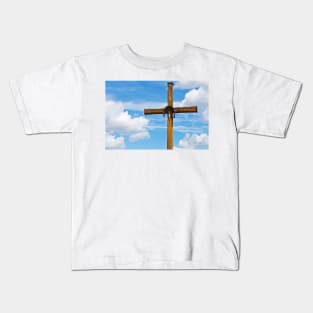 Figurine of Jesus Christ on a wooden cross against under blue cloudy sky Kids T-Shirt
